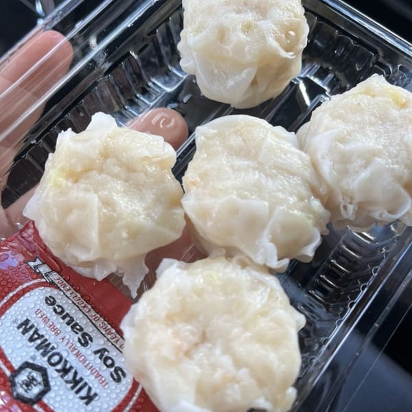 Five Japanese shumai dumplings in a plastic container with a Kikkoman soy sauce packet.