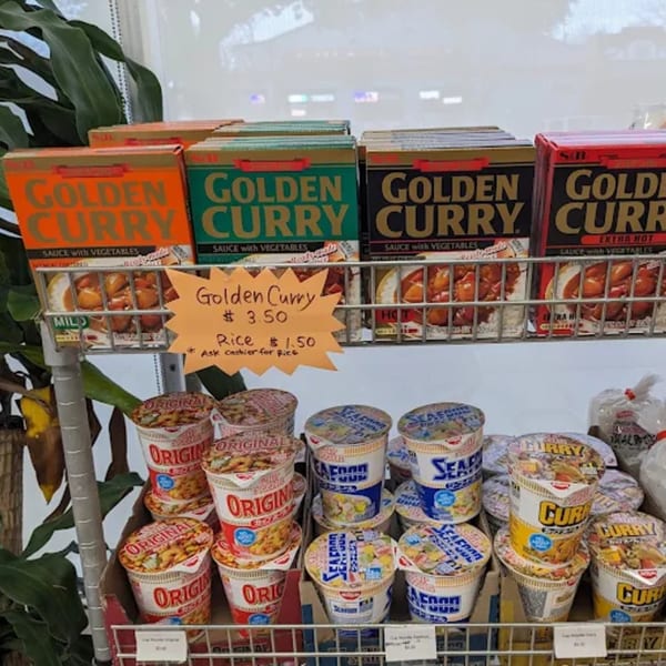 A store shelf displays various Japanese curry boxes and instant noodle cups for sale.